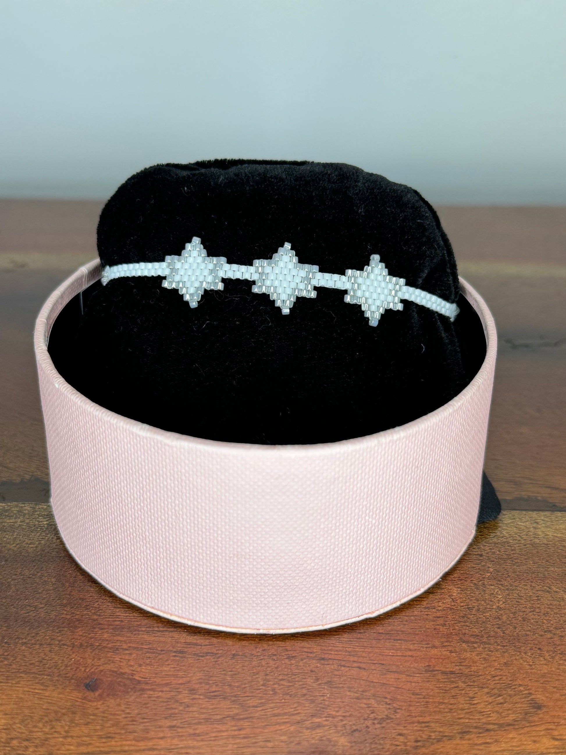 A bracelet with purple and gold colors displayed on a black cushion inside a pink box.