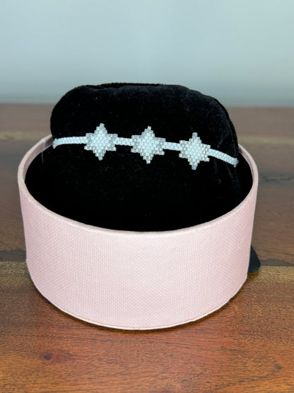 A bracelet with purple and gold colors displayed on a black cushion inside a pink box.