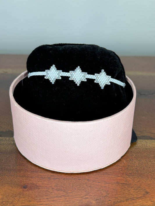 A bracelet with purple and gold colors displayed on a black cushion inside a pink box.