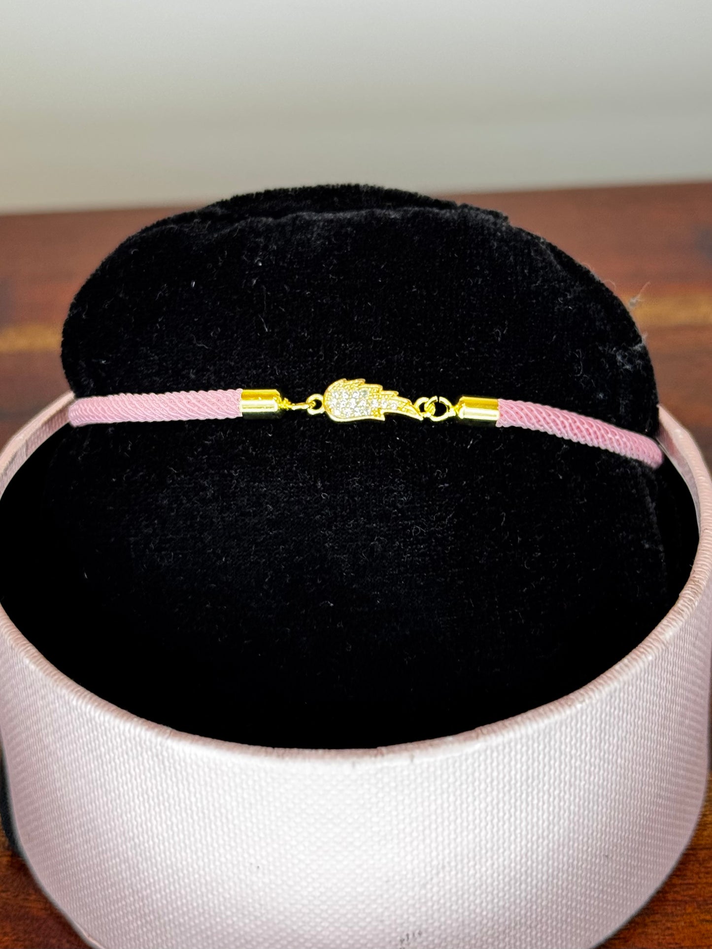 Pink bracelet with gold clasp on a black cushion inside a white box
