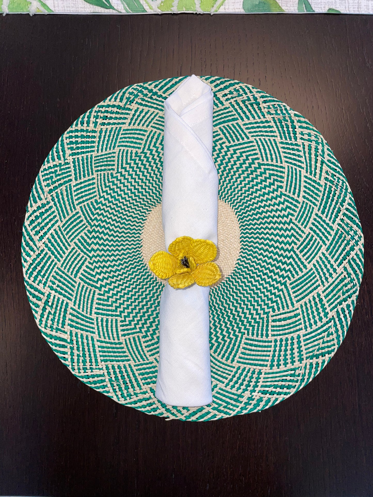 A green napkin ring with a yellow floral pattern, displaying a napkin neatly rolled and placed in the center.