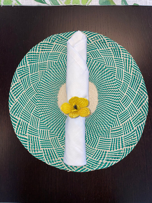 A green napkin ring with a yellow floral pattern, displaying a napkin neatly rolled and placed in the center.